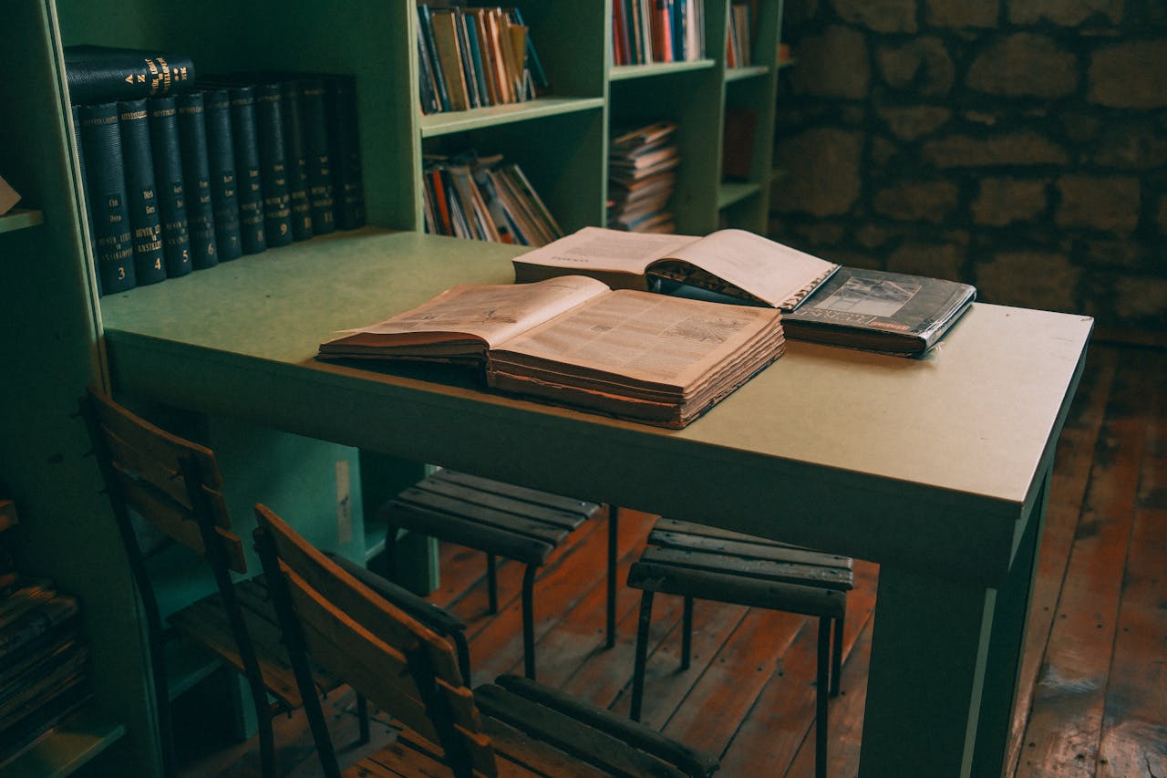 Warm-toned library interior featuring open books on a vintage table with green shelves.